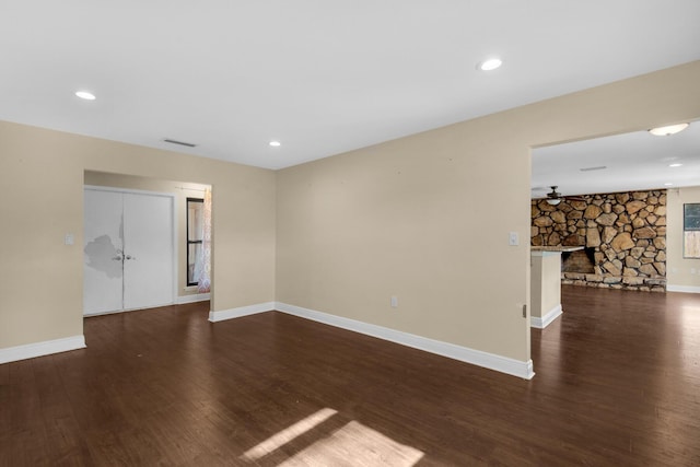 empty room featuring dark wood-type flooring, visible vents, a fireplace, and baseboards