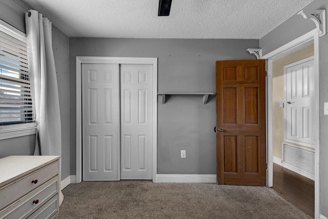 unfurnished bedroom with a textured ceiling, dark colored carpet, a closet, and baseboards