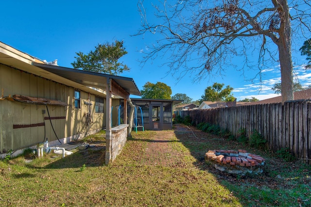 view of yard featuring a sunroom, a fenced backyard, and a fire pit