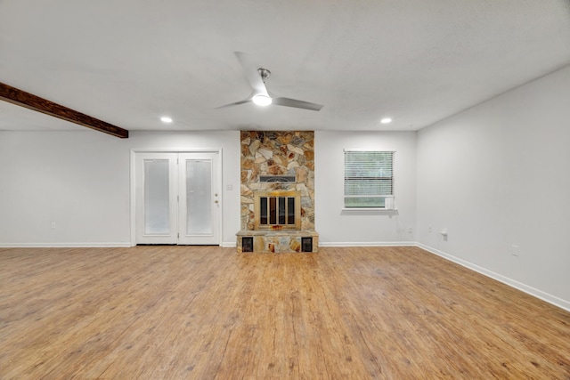 unfurnished living room featuring beam ceiling, a stone fireplace, ceiling fan, and light hardwood / wood-style flooring