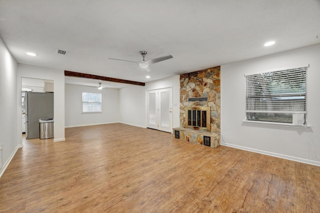 unfurnished living room featuring ceiling fan, light hardwood / wood-style floors, a stone fireplace, and beam ceiling