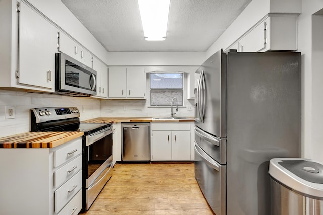 kitchen with white cabinets, sink, a textured ceiling, light hardwood / wood-style floors, and stainless steel appliances