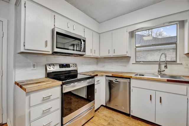 kitchen featuring appliances with stainless steel finishes, a textured ceiling, sink, light hardwood / wood-style floors, and white cabinetry