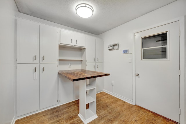 kitchen featuring white cabinets, wooden counters, a textured ceiling, and light wood-type flooring