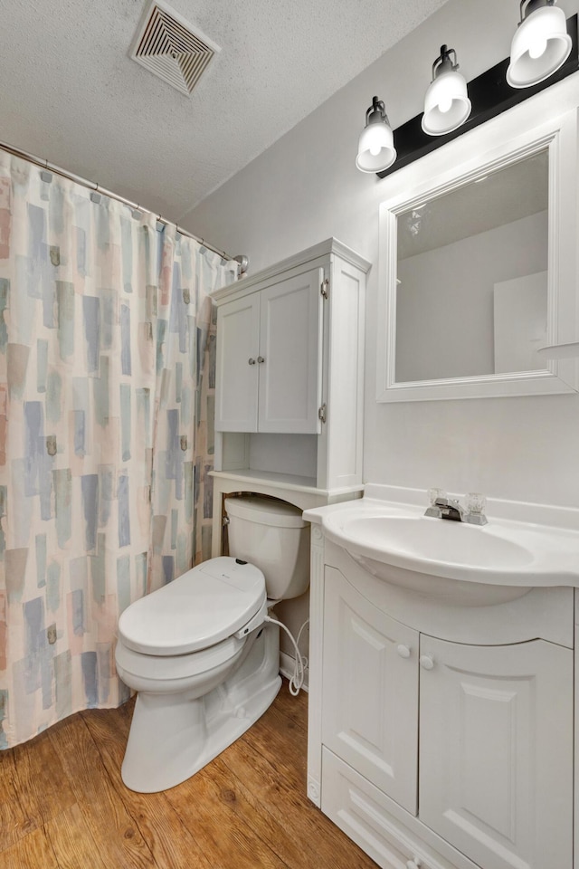 bathroom featuring a shower with curtain, wood-type flooring, a textured ceiling, toilet, and vanity