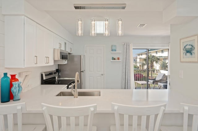 kitchen with sink, range with electric stovetop, decorative light fixtures, a kitchen bar, and white cabinets