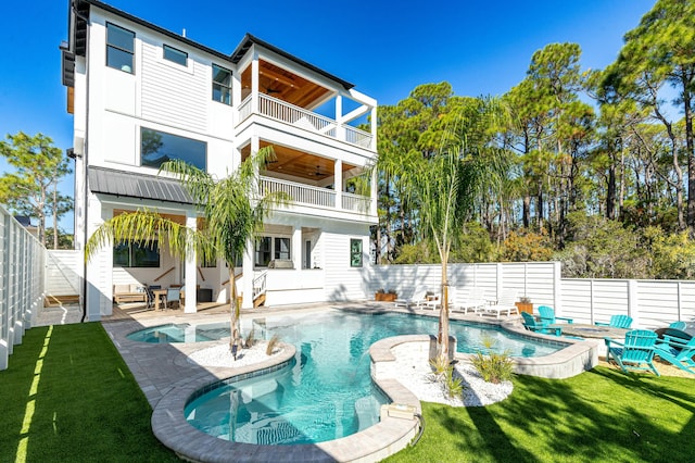 rear view of property featuring a pool with hot tub, a lawn, a patio, and a balcony