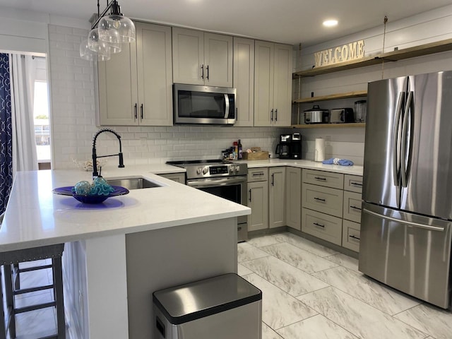 kitchen featuring pendant lighting, a breakfast bar, gray cabinetry, backsplash, and appliances with stainless steel finishes