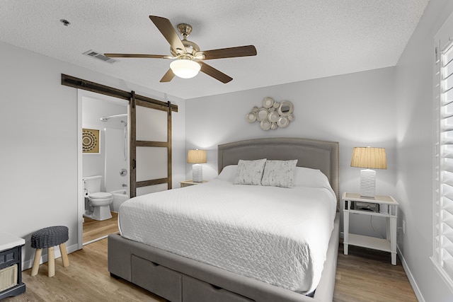 144 Spires Ln Unit 114, Santa Rosa Beach, FL 32459 - bedroom with ensuite bath, a barn door, a textured ceiling, and light wood-type flooring