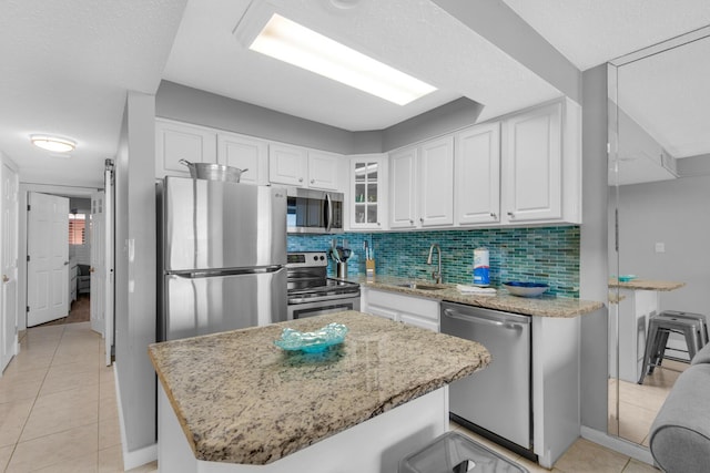 kitchen featuring stainless steel appliances, a center island, sink, white cabinetry, and light tile patterned flooring