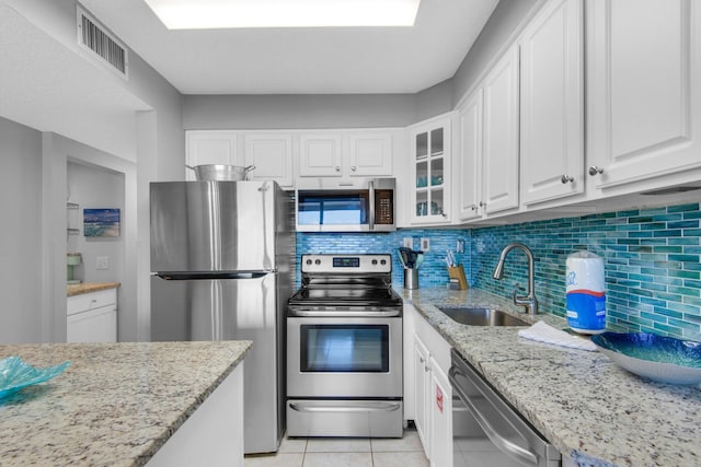 kitchen with light stone counters, light tile patterned floors, white cabinets, appliances with stainless steel finishes, and sink