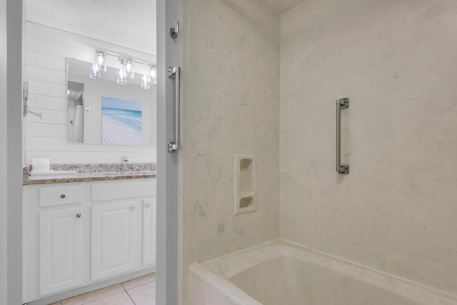 bathroom with tile patterned flooring, a textured ceiling, tiled shower / bath combo, and vanity