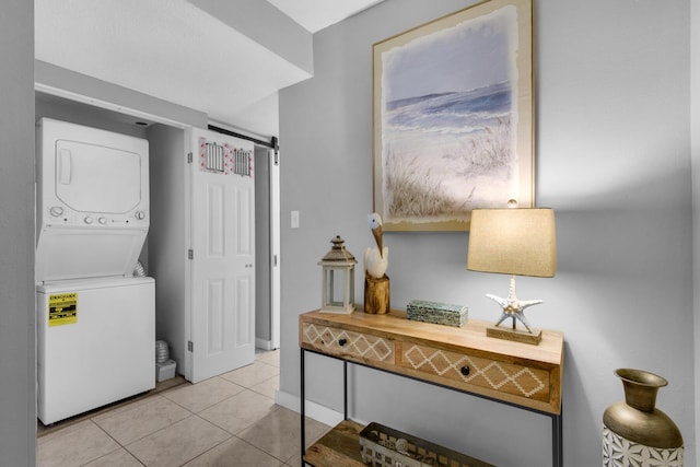 laundry room featuring stacked washing maching and dryer, light tile patterned flooring, and a barn door