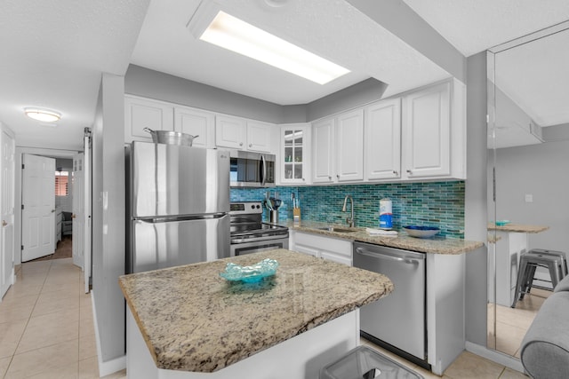 kitchen with sink, white cabinetry, a center island, light tile patterned floors, and appliances with stainless steel finishes