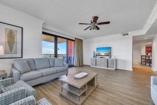 living room featuring crown molding, light hardwood / wood-style flooring, ceiling fan, and a textured ceiling