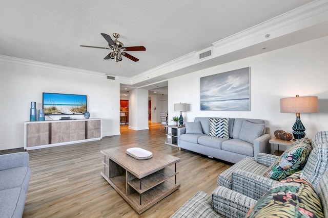 living room with a textured ceiling, ceiling fan, wood-type flooring, and crown molding