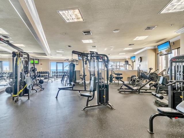 gym with a healthy amount of sunlight, a textured ceiling, and ornamental molding