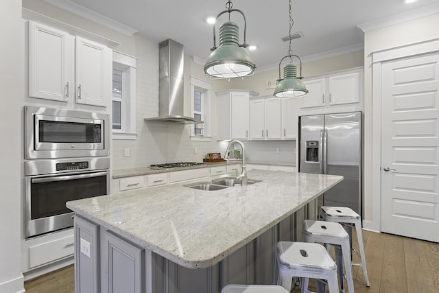 kitchen featuring appliances with stainless steel finishes, sink, an island with sink, and wall chimney range hood