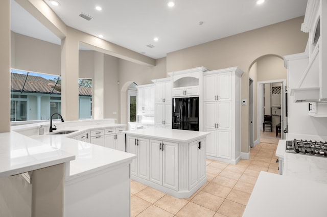 kitchen with sink, a kitchen island, black fridge, kitchen peninsula, and white cabinets