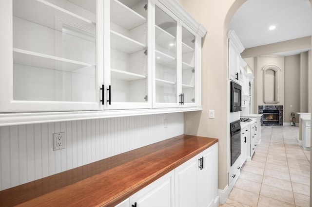 bar with white cabinetry, a high end fireplace, butcher block countertops, light tile patterned floors, and black appliances