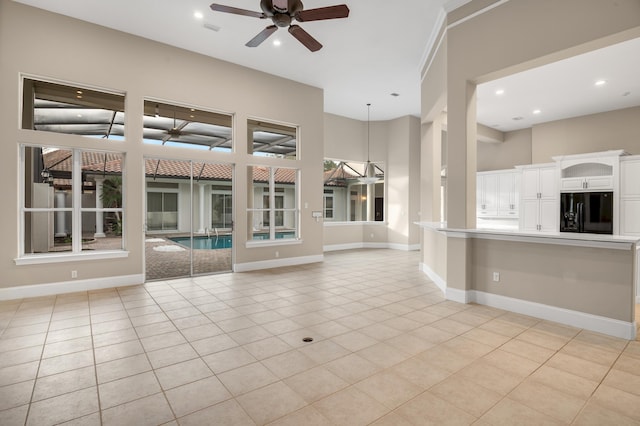 unfurnished living room with ceiling fan, light tile patterned floors, and a towering ceiling