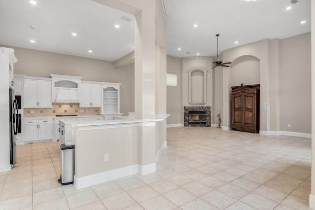 kitchen with stainless steel refrigerator, ceiling fan, a fireplace, a center island with sink, and white cabinets