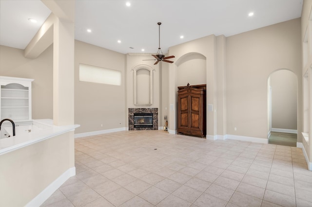 unfurnished living room with ceiling fan, light tile patterned floors, a fireplace, and a high ceiling