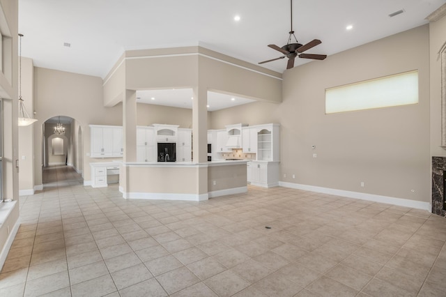 kitchen with a center island, ceiling fan with notable chandelier, black refrigerator, a towering ceiling, and custom range hood