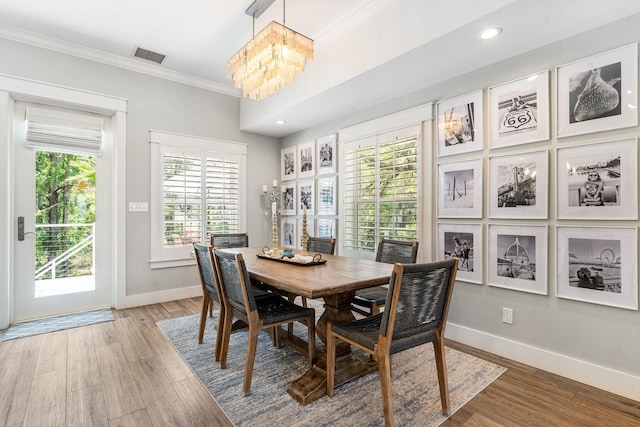 dining area with hardwood / wood-style flooring, crown molding, and an inviting chandelier