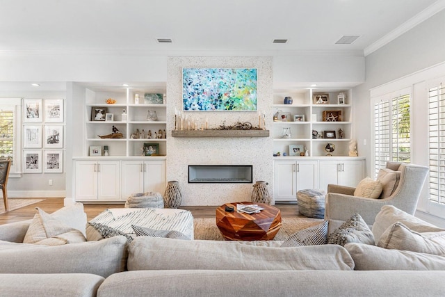 living room featuring a fireplace, ornamental molding, light hardwood / wood-style flooring, and built in features