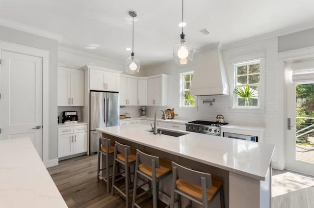 kitchen featuring white cabinetry, sink, stainless steel appliances, a breakfast bar area, and custom range hood