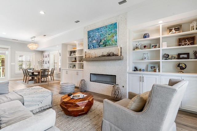 living room featuring built in shelves, light hardwood / wood-style floors, ornamental molding, and a fireplace