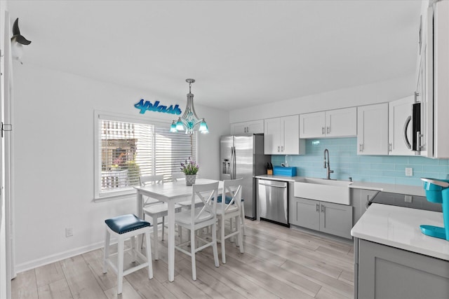 kitchen with backsplash, hanging light fixtures, sink, appliances with stainless steel finishes, and light hardwood / wood-style floors