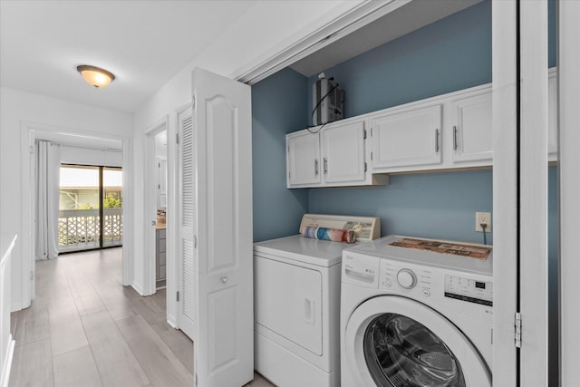 clothes washing area with washer and dryer, light hardwood / wood-style floors, and cabinets