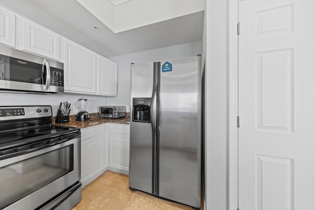 kitchen featuring white cabinets, light tile patterned floors, appliances with stainless steel finishes, and dark stone counters