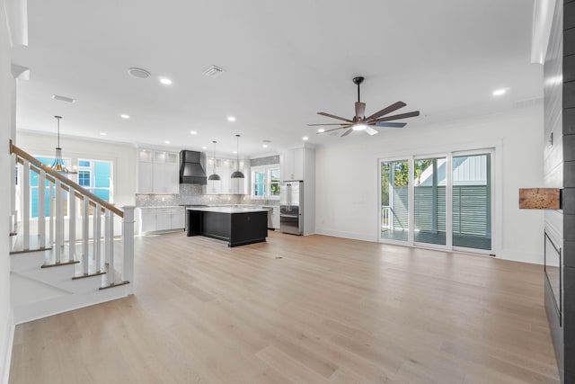 unfurnished living room featuring ceiling fan with notable chandelier, light hardwood / wood-style flooring, a wealth of natural light, and ornamental molding