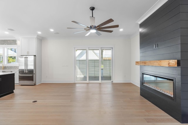 unfurnished living room with light wood-type flooring, a large fireplace, ceiling fan, crown molding, and sink