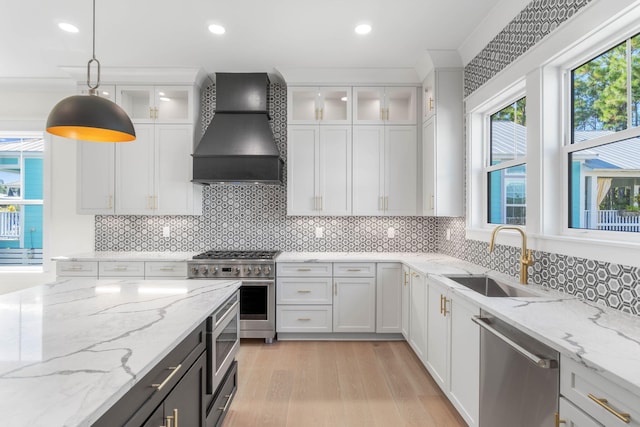 kitchen with custom range hood, stainless steel appliances, sink, white cabinets, and hanging light fixtures