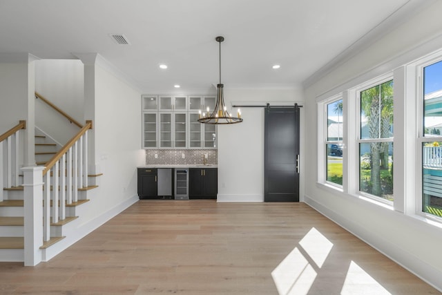 kitchen with backsplash, beverage cooler, crown molding, a barn door, and decorative light fixtures