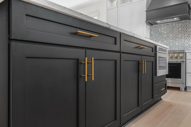 room details with backsplash, premium range hood, light stone counters, white cabinets, and stainless steel electric range