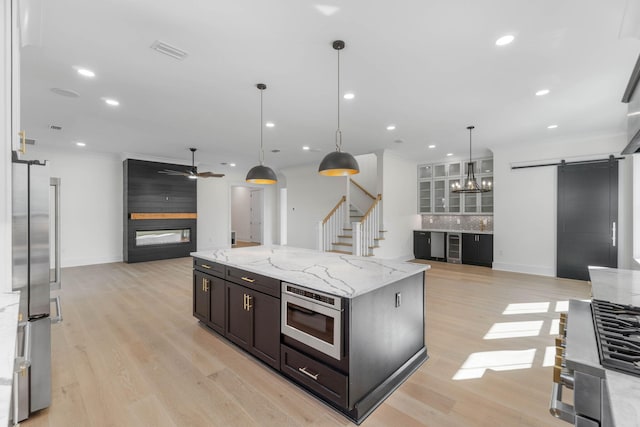 kitchen featuring ceiling fan, light stone countertops, hanging light fixtures, tasteful backsplash, and a barn door