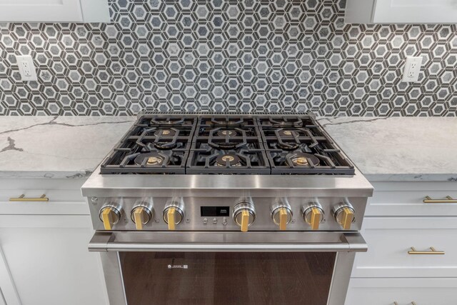 interior details featuring light stone counters, white cabinetry, high end stainless steel range oven, and tasteful backsplash