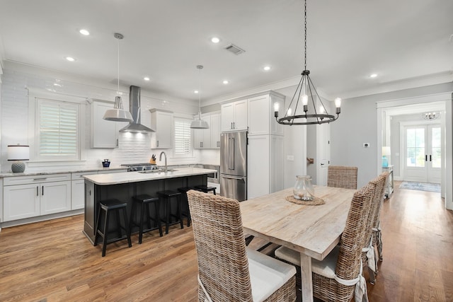 dining room featuring french doors, sink, an inviting chandelier, light hardwood / wood-style flooring, and ornamental molding