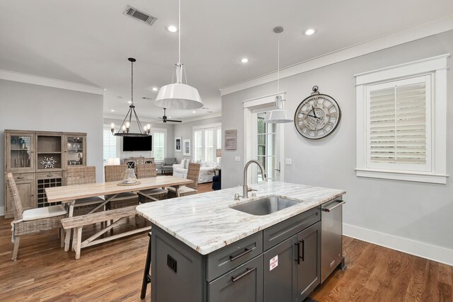 kitchen with sink, hanging light fixtures, gray cabinets, an island with sink, and light stone counters