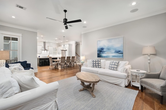 living room featuring hardwood / wood-style floors, ceiling fan with notable chandelier, and crown molding