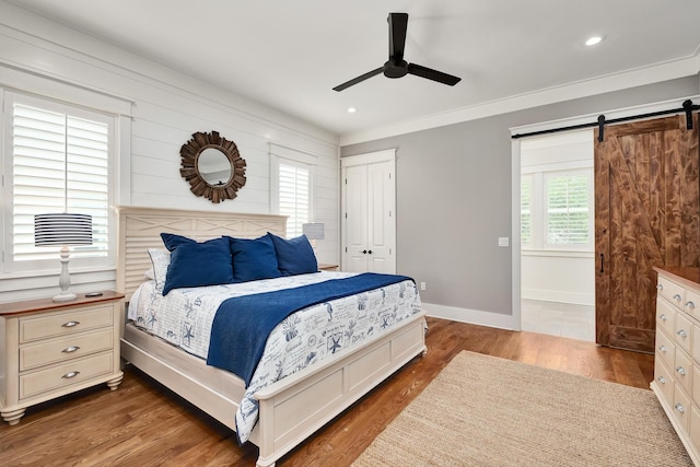 bedroom with crown molding, ceiling fan, a barn door, dark hardwood / wood-style floors, and a closet