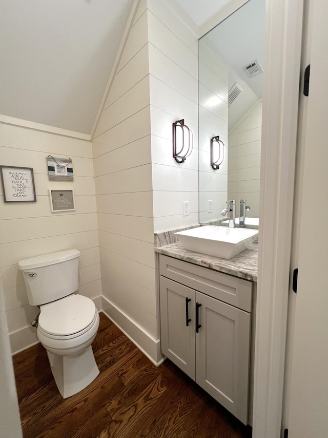 bathroom featuring wood-type flooring, vanity, toilet, and lofted ceiling