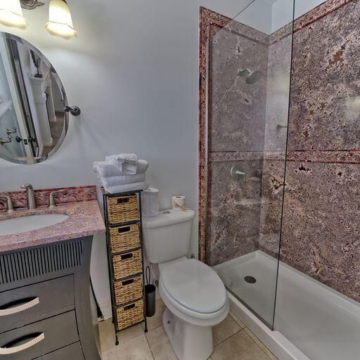 bathroom with tile patterned floors, vanity, toilet, and tiled shower