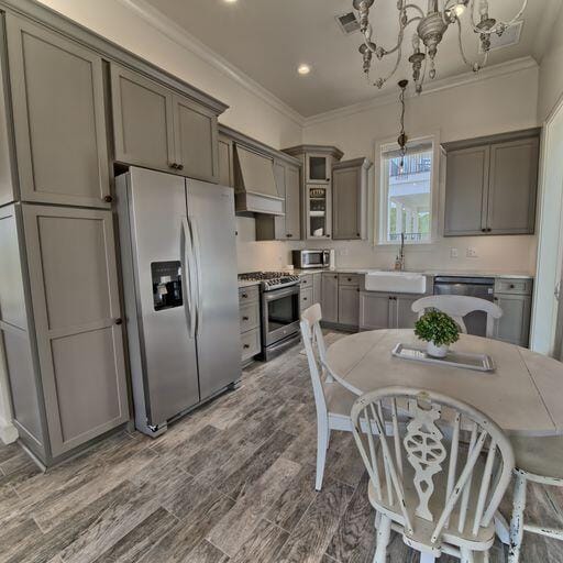 kitchen with appliances with stainless steel finishes, premium range hood, sink, a chandelier, and hanging light fixtures