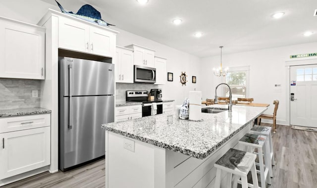 kitchen with backsplash, white cabinetry, appliances with stainless steel finishes, and a center island with sink